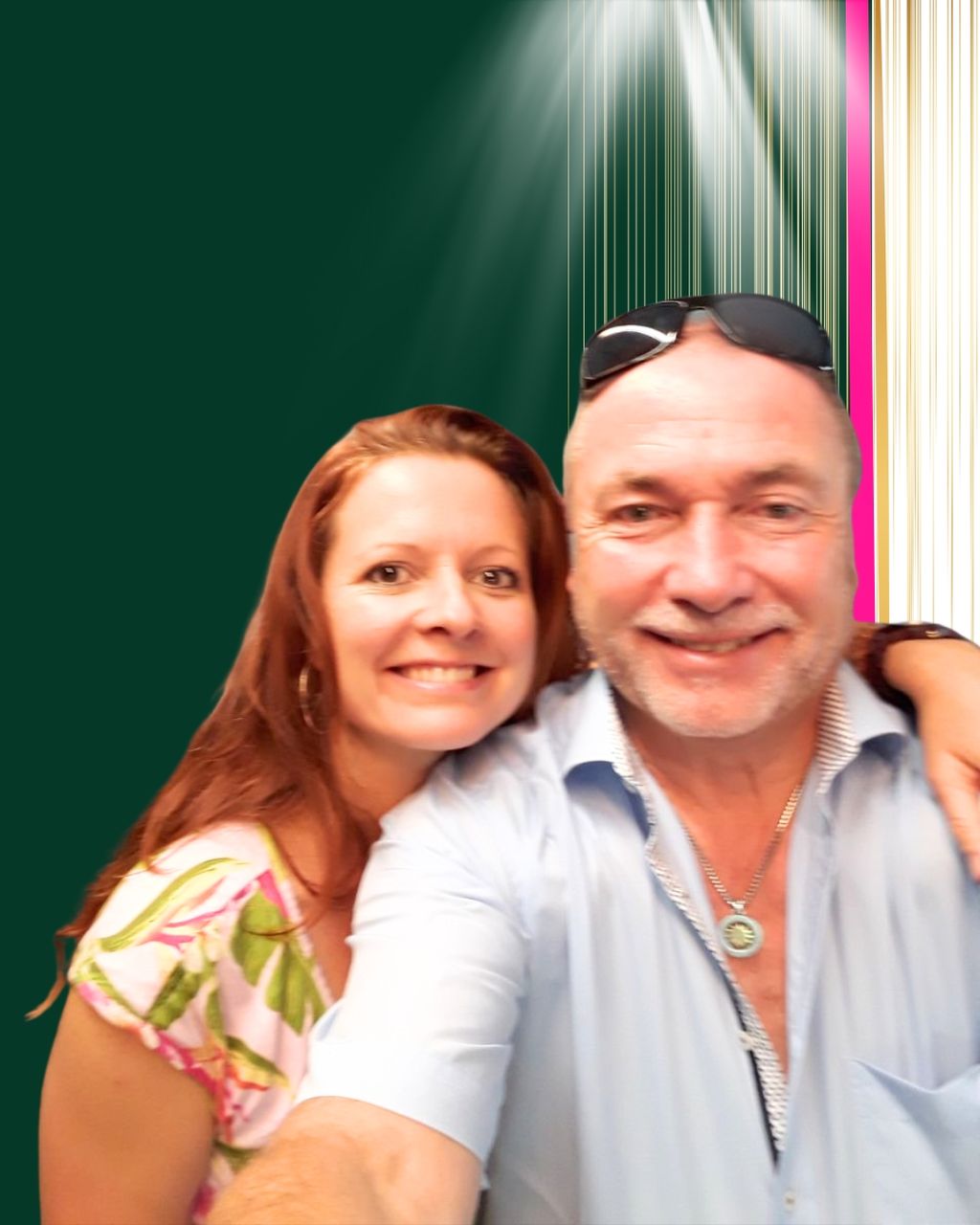 Ein Mann und eine Frau stehen nah beieinander und lächeln in die Kamera vor einem grünen Hintergrund mit vertikalen Streifen und Lichtstrahlen.